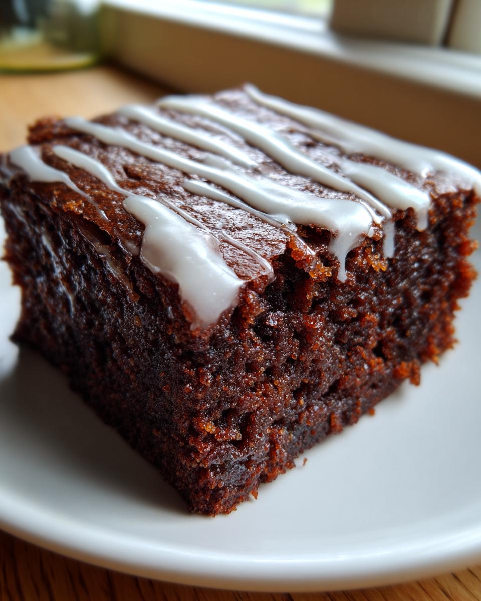 Close-up of a rich, dark square of gingerbread brownies drizzled with white vanilla icing.