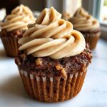 A close-up of one decadent pecan pie cupcake topped with a swirl of light brown, speckled frosting.
