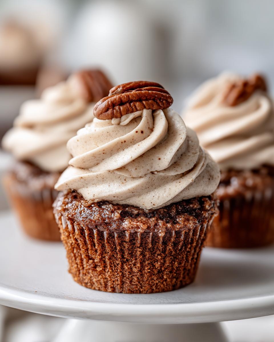 A close-up of one decadent pecan pie cupcake topped with spiced frosting and a whole pecan half.