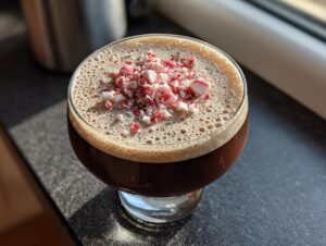 Close-up of a rich peppermint espresso martini topped with frothy foam and crushed candy canes.