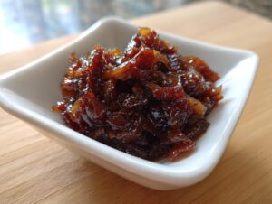Close-up of rich, dark brown caramelized onions served in a small white square bowl on a wooden surface.