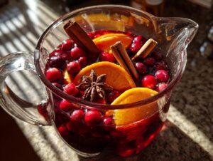Close-up of a glass pitcher filled with vibrant red holiday sangria, garnished with fresh cranberries, orange slices, cinnamon sticks, and star anise.