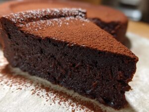 Close-up of a decadent slice of flourless chocolate torte, intensely dark and topped with cocoa powder.