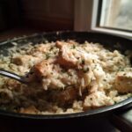 A spoonful of creamy one pot chicken and rice, garnished with parsley, lifted from the skillet.