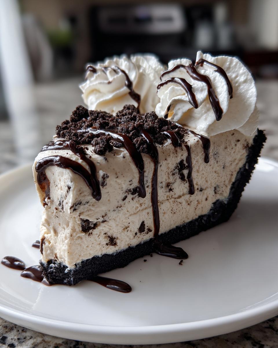 A decadent slice of cookies and cream ice cream pie with a dark crust, topped with whipped cream and chocolate syrup.