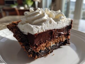 A decadent slice of chocolate mud pie featuring a dark crust, rich chocolate filling, and a generous topping of whipped cream.