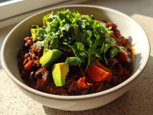 A close-up of a hearty bowl of smoky black bean chili, garnished generously with fresh cilantro and chunks of avocado.