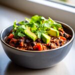 A close-up of a bowl of rich, dark black bean chili topped with fresh avocado slices and cilantro.