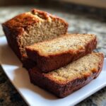 Close-up of moist sourdough banana bread loaf with two thick slices stacked on a white serving plate.