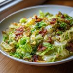 A close-up of a bowl filled with Southern Fried Cabbage recipe, featuring wilted green cabbage and crispy bacon pieces.