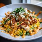 A close-up of a delicious street corn chicken rice bowl topped with crumbled cheese, cilantro, and a creamy orange sauce.