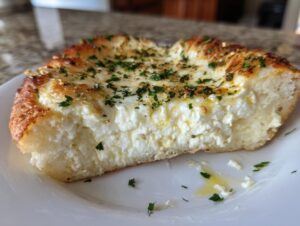Thick slice of homemade white pizza showing a generous layer of creamy ricotta cheese and golden crust, topped with herbs.