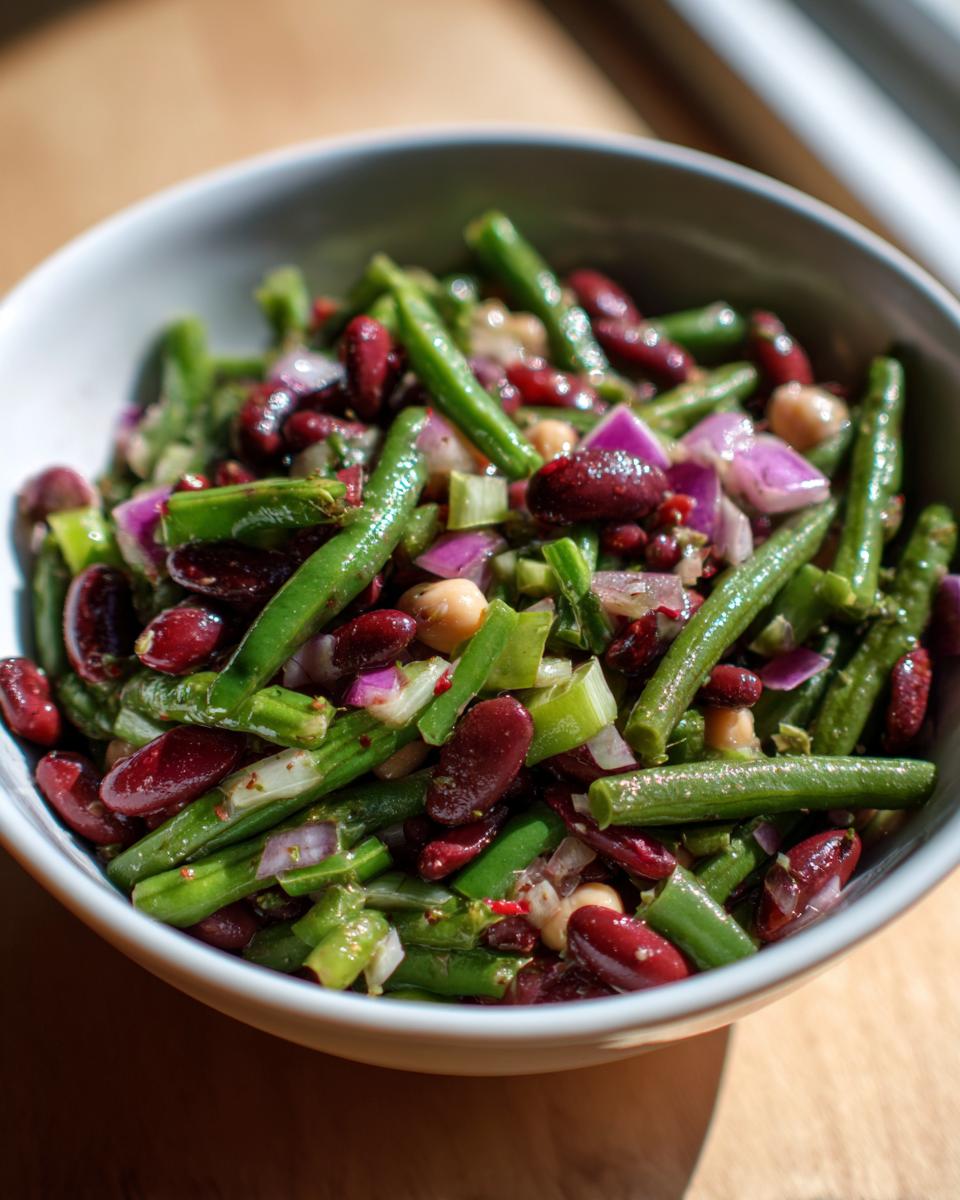 Close-up of a vibrant bean salad featuring green beans, kidney beans, and red onion in a white bowl.