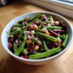 Close-up of a vibrant bean salad featuring green beans, kidney beans, and chickpeas, mixed with red onion.