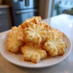 A pile of golden, star-shaped whipped shortbread cookies stacked on a white plate.