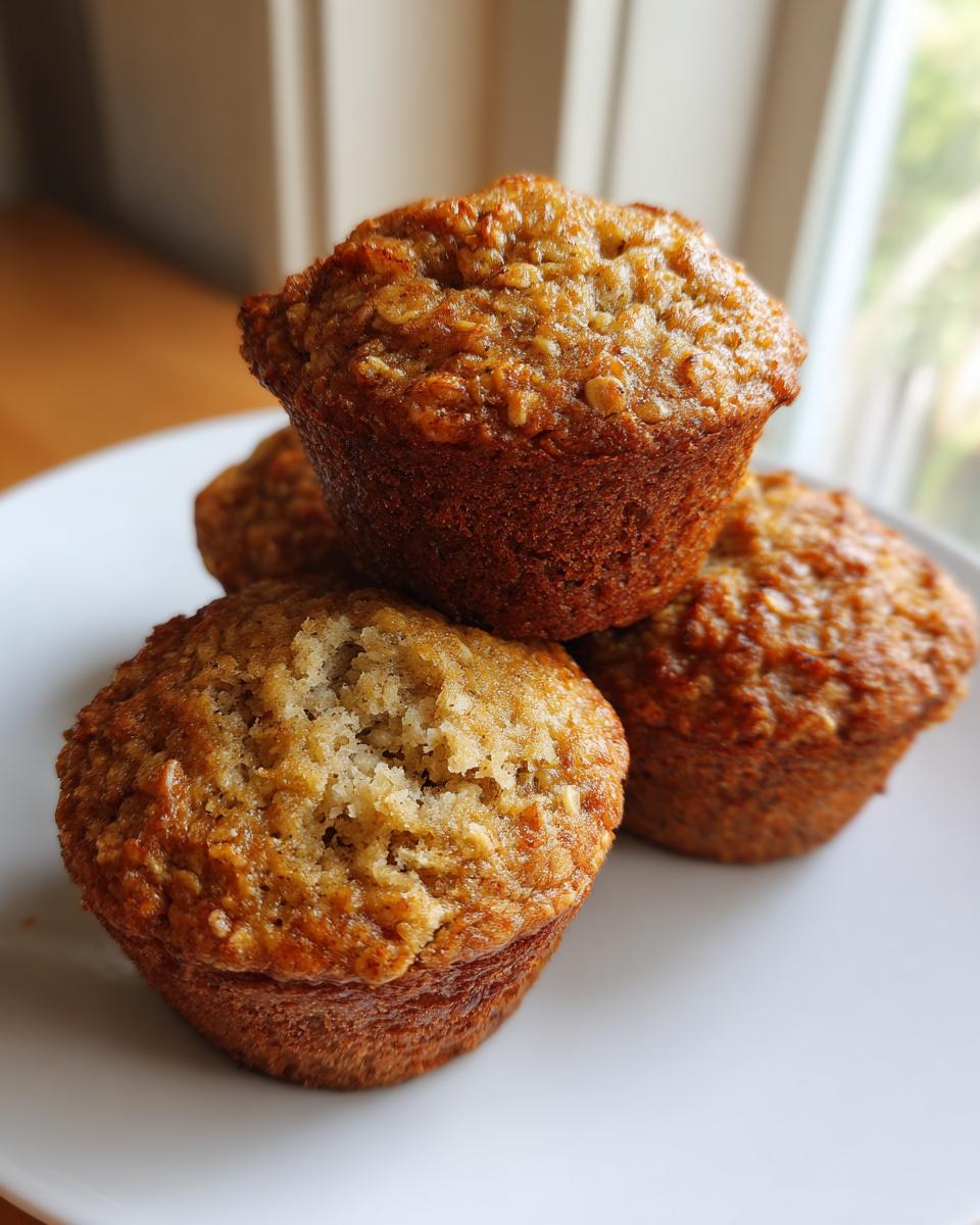 A stack of four golden-brown banana oatmeal muffins with visible oats on a white plate.