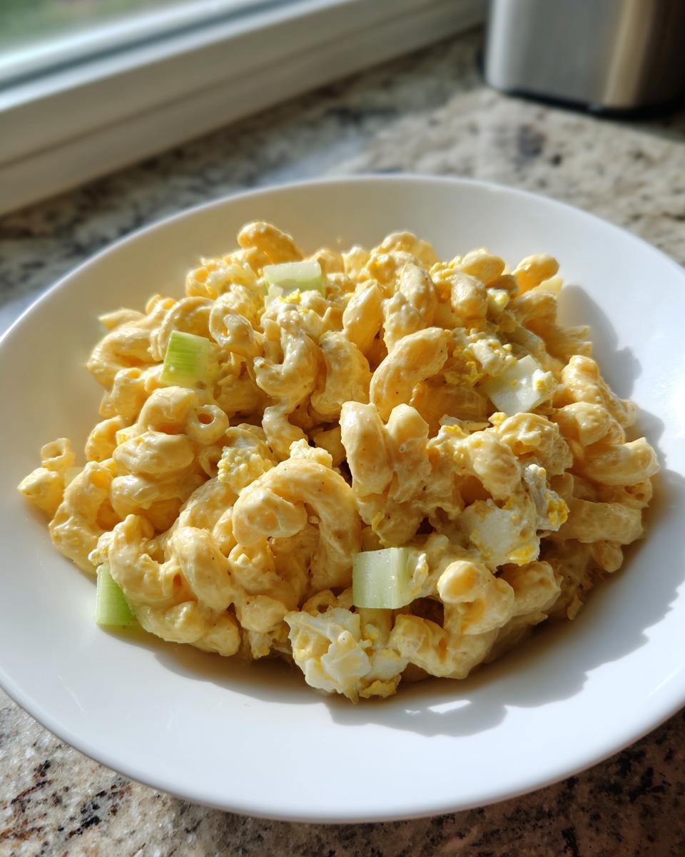 A white bowl filled with creamy, sweet amish macaroni salad featuring elbow pasta, chopped eggs, and visible chunks of celery.