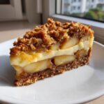 A perfect slice of apple crumble cheesecake showing layers of crust, apples, cream cheese, and crumble topping.