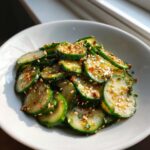 Close-up of thinly sliced cucumbers tossed in a savory dressing and topped with toasted sesame seeds for an asian cucumber salad.