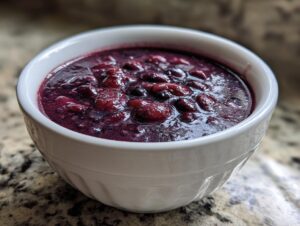 Close-up of a white bowl filled with thick, dark purple black bean soup, showing whole beans.