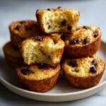 A stack of golden brown chocolate chip pancake muffins, with two on top broken open to show the fluffy interior.