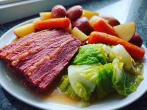 A plate featuring sliced corned beef and cabbage, served with boiled carrots and potatoes.