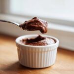 A spoonful of rich cottage cheese chocolate mousse being lifted from a small white ramekin.