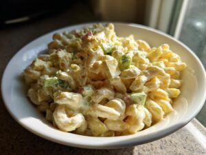 A close-up of creamy amish macaroni salad mixed with celery and eggs served in a white bowl.
