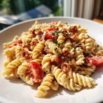 Close-up of creamy blt pasta salad featuring fusilli pasta, crispy bacon bits, and halved cherry tomatoes.