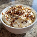 A white bowl filled with creamy caramelized onion dip, topped generously with dark, rich caramelized onions.