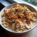 A bowl of creamy chicken parmesan soup featuring shredded chicken, pasta, and a generous topping of toasted breadcrumbs and herbs.