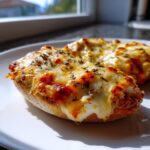 Close-up of two halves of crispy English muffin pizza topped with melted, browned cheese and herbs.