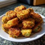 A mound of golden brown, crispy fried okra pieces piled high on a white plate, ready to eat.