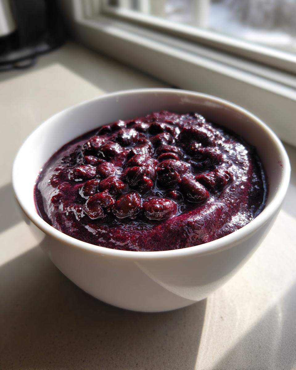 A thick, dark purple berry mixture, possibly a smoothie or compote, topped with whole berries in a white bowl.