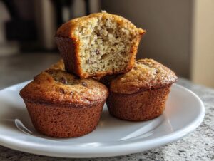 A stack of golden brown protein muffins, one cut in half showing the moist interior and chocolate chips.