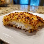 A close-up cross-section of a perfectly cooked parmesan crusted tilapia fillet showing flaky white fish inside and a golden, crispy topping.