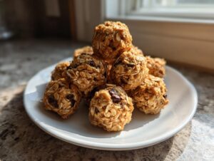 A small pile of homemade peanut butter protein balls made with oats and chocolate chips sits on a white plate.