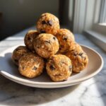 A stack of homemade peanut butter protein balls mixed with oats and mini chocolate chips sitting on a light plate.