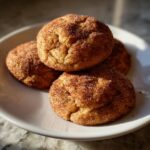 Close-up of three soft pumpkin snickerdoodles coated in cinnamon sugar stacked on a white plate.
