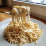 A fork lifts spaghetti coated in creamy cottage cheese alfredo sauce, showing long, tempting cheese stretches.