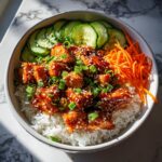 Close-up of a delicious salmon bowl featuring glazed salmon pieces over white rice, topped with sesame seeds, green onions, cucumbers, and shredded carrots.