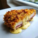 Cross-section of a perfectly cooked chicken cordon bleu showing crispy breading, ham, and melted cheese sauce oozing out.