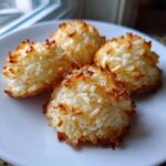 Close-up of four perfectly baked coconut cookies with toasted edges on a white plate.