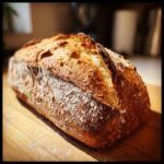 A freshly baked loaf of crusty bread with a deeply scored, golden-brown top dusted with flour.