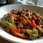 A close-up, appetizing serving of amazing ground beef stir fry mixed with bright green broccoli florets and red bell peppers.