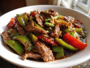 A close-up of savory pepper steak stir-fry featuring beef strips, green and red bell peppers, and a rich sauce.