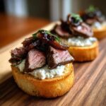Close-up of a perfectly prepared steak crostini topped with medium-rare steak, creamy blue cheese spread, and caramelized onions.