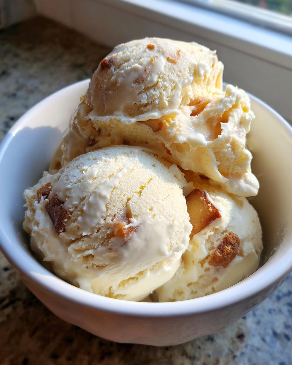 Three scoops of creamy apple pie ice cream loaded with pie crust pieces served in a white bowl.