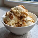 Three scoops of creamy apple pie ice cream topped with cinnamon crumble pieces in a white bowl.