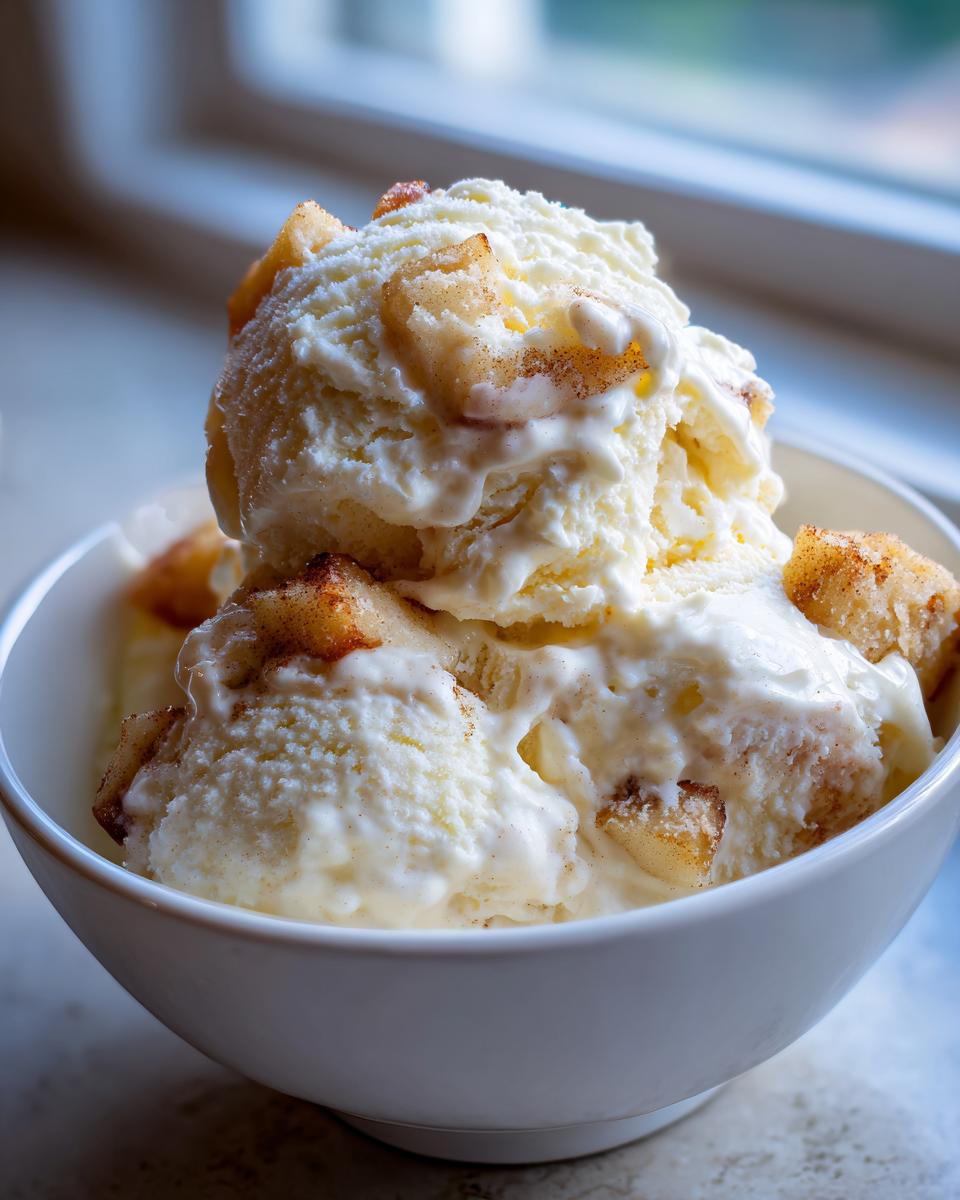 Close-up of creamy vanilla apple pie ice cream scoops topped with spiced apple pieces in a white bowl.